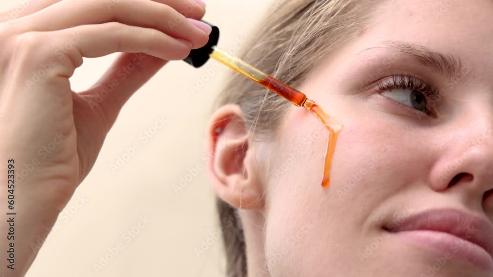 woman applying on face finger vitamin c serum pink color liquid.face care anti wrinkle acne aging procedures.young female applying with finger on cheek. 4k. drops falling from pipette
