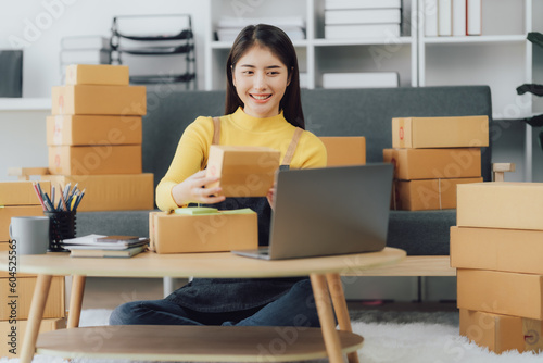 tarting Small business entrepreneur SME freelance,Portrait young woman working at home office, BOX,smartphone,laptop, online, marketing, packaging, delivery, SME, e-commerce concept © Kritdanai