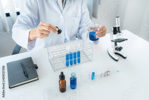 Scientist woman holding beaker and dropper to dropping blue liqu