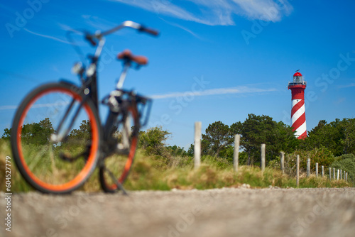 Dutch lighthouse red white against blue sky. Comfort bicycle out of focus on stony path. Sunny summer afternoon. Netherlands, Zeeland, Haamstede.