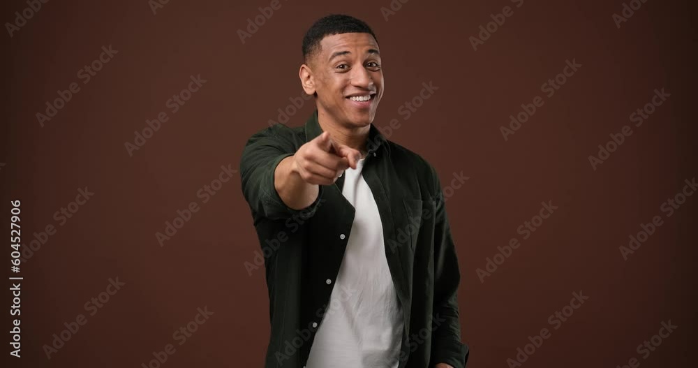 Playful african american guy pointing at camera and smiling standing over brown studio background