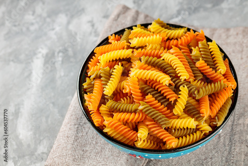 Fusilli dry pasta in bowl on concrete. Colorful italian raw pasta on a linen napkin. Copy space