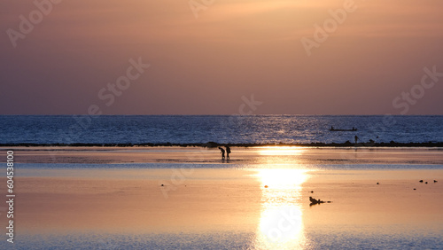 Golden sunset sunlight reflecting over glimmering ocean with silhouetted people fishing in Timor-Leste, Southeast Asia © Adam Constanza