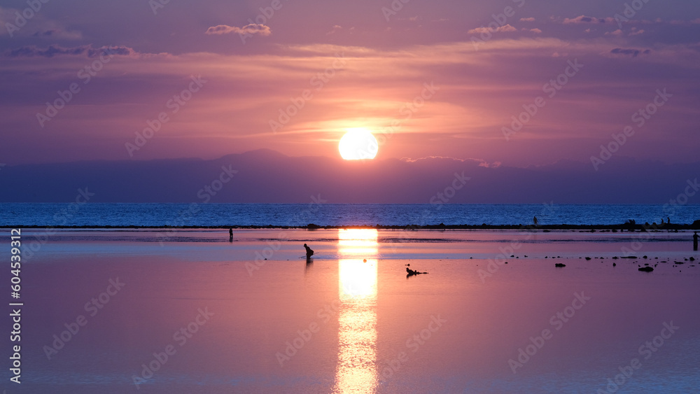 Silhouetted fishermen gleaning and fishing for seafood at low tide with stunning pink purple sunset reflecting over Indo-Pacific ocean in Timor-Leste