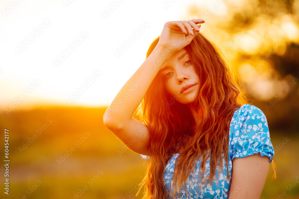 Young woman in stylish summer dress feeling free in the field with flowers at sunset. Nature, fashion, vacation and lifestyle