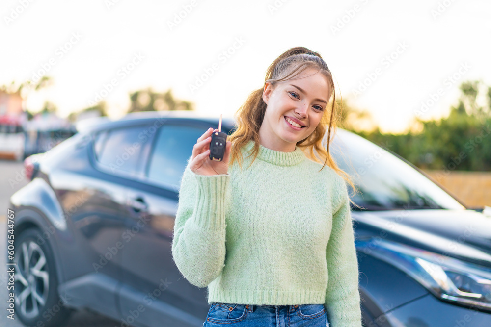Young pretty girl holding car keys at outdoors smiling a lot - obrazy, fototapety, plakaty 