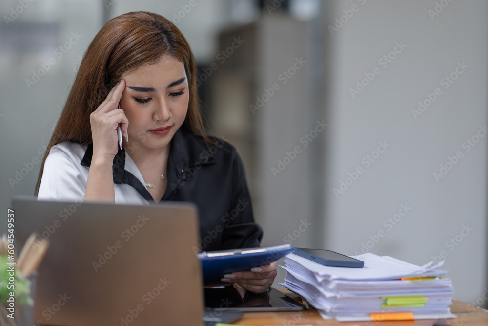 Portrait of tired young business Asian woman work with documents tax laptop computer in office. Sad, unhappy, Worried, Depression, or employee life stress concept Portrait of tired young business Asian woman work with documents tax laptop computer in office. Sad, unhappy, Worried, Depression, or employee life stress concept