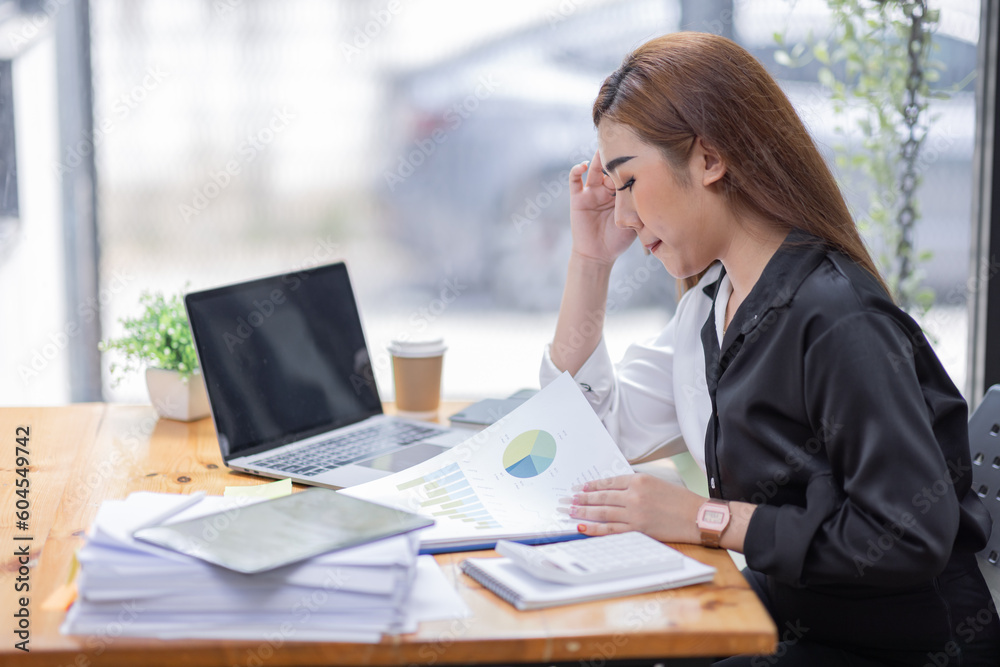 Portrait of tired young business Asian woman work with documents tax laptop computer in office. Sad, unhappy, Worried, Depression, or employee life stress concept Portrait of tired young business Asian woman work with documents tax laptop computer in office. Sad, unhappy, Worried, Depression, or employee life stress concept