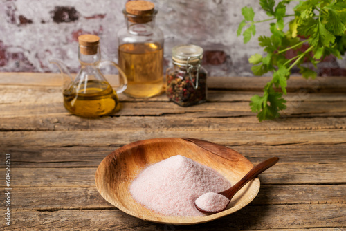 Wooden plate with pink salt, on a rustic wooden table with jars of pepper, vinegar and olive oil, close-up.