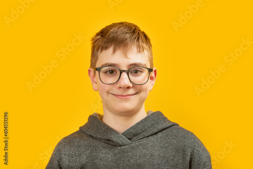 Portrait of brunette boy with brown eyes with glasses on yellow background. Teenager with brown hair looks into the camera and smiles