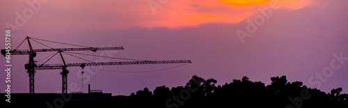 A blue slan surrounds the building under construction. Crane. Crane for lifting things in construction against sunset sky atmosphere. communities and large industrial construction zones.	 photo