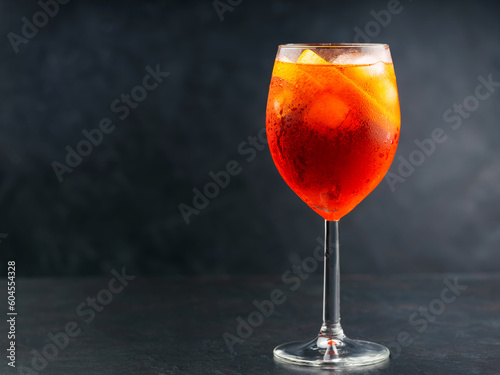 Aperol Spritz cocktail in glass with fresh orange on dark background. Glass of ice cold Aperol Spritz cocktail served in a wine glass. Copy space