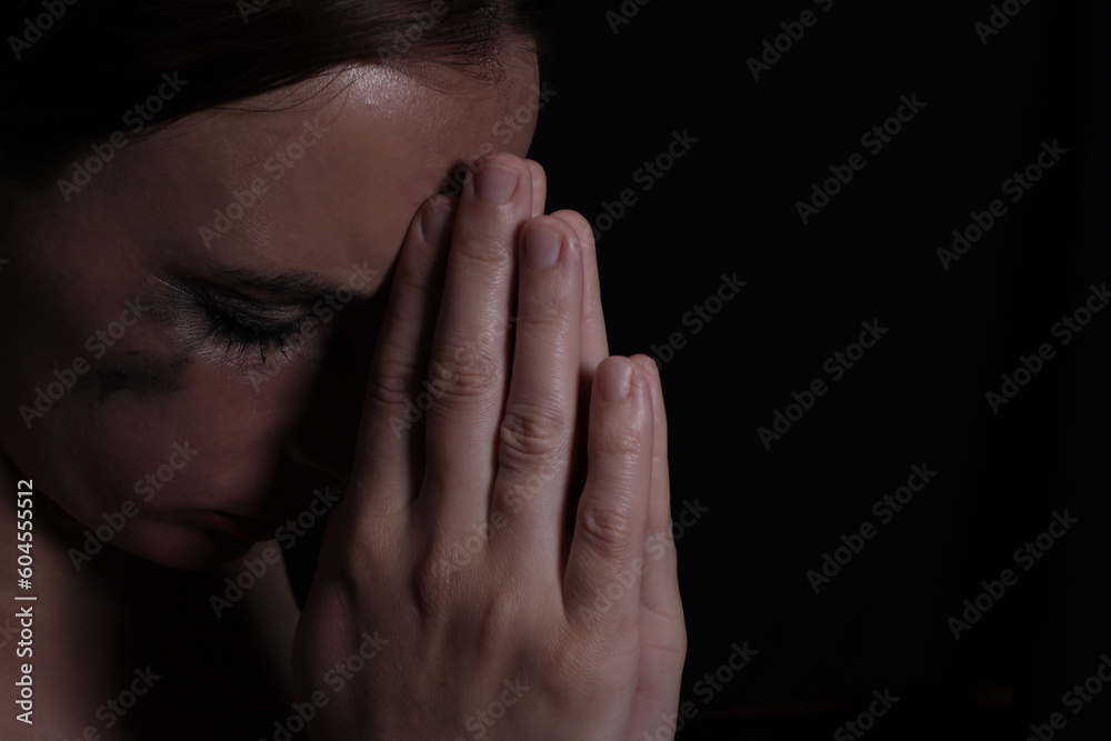 Portrait of a young crying woman with smeared mascara and lipstick praying on a black background Portrait of a young crying woman with smeared mascara and lipstick praying on a black background