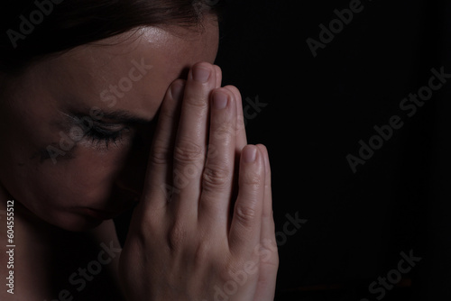 Portrait of a young crying woman with smeared mascara and lipstick praying on a black background