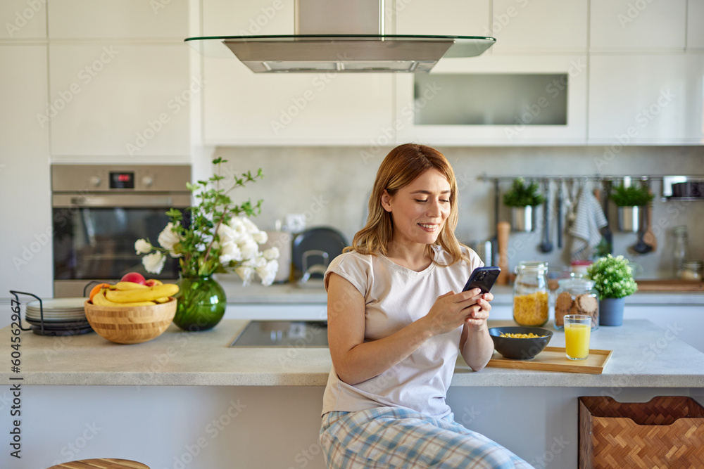 Portrait of a woman eating breakfast while using mobile phone in the kitchen at home Portrait of a woman eating breakfast while using mobile phone in the kitchen at home