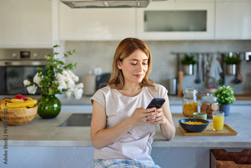 Portrait of a woman eating breakfast while using mobile phone in the kitchen at home Portrait of a woman eating breakfast while using mobile phone in the kitchen at home