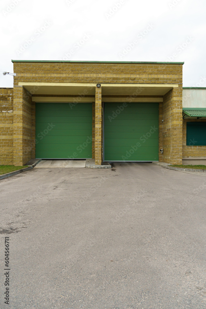 A large modern garage made of beige brick and green roller gates. Video surveillance system at the entrance to the garage. Safe conditions for storing cars and property.