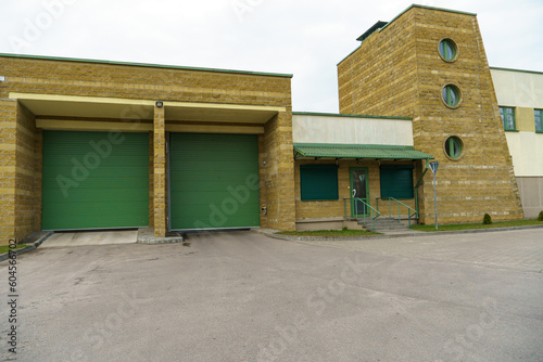Fototapeta Naklejka Na Ścianę i Meble -  A large modern garage made of beige brick and green roller gates. Video surveillance system at the entrance to the garage. Safe conditions for storing cars and property.
