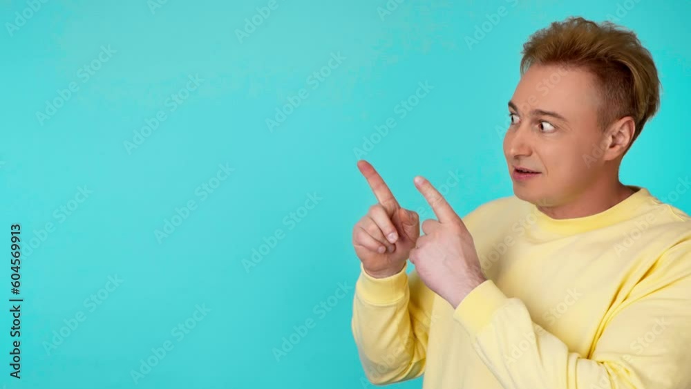 Face, man and pointing to mockup, advertising, branding in studio isolated on blue background. Smiling guy male showing product placement, empty place or mock up space, marketing in yellow sweatshirt Face, man and pointing to mockup, advertising, branding in studio isolated on blue background. Smiling guy male showing product placement, empty place or mock up space, marketing in yellow sweatshirt