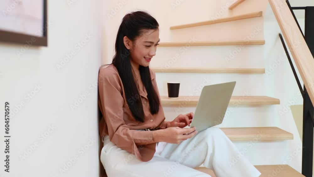 Drinking coffee. Asian business working woman work online job on laptop computer, sitting on stairs at smallbusiness home office. Work from home