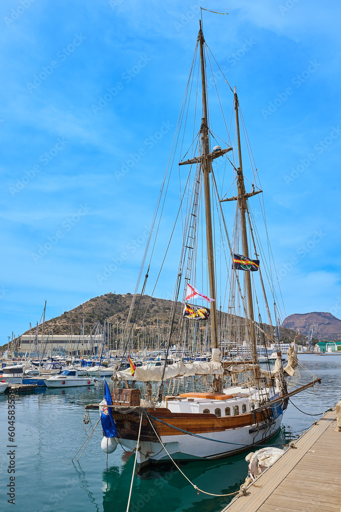 A sailing ship with two masts stands at the pier in the marina