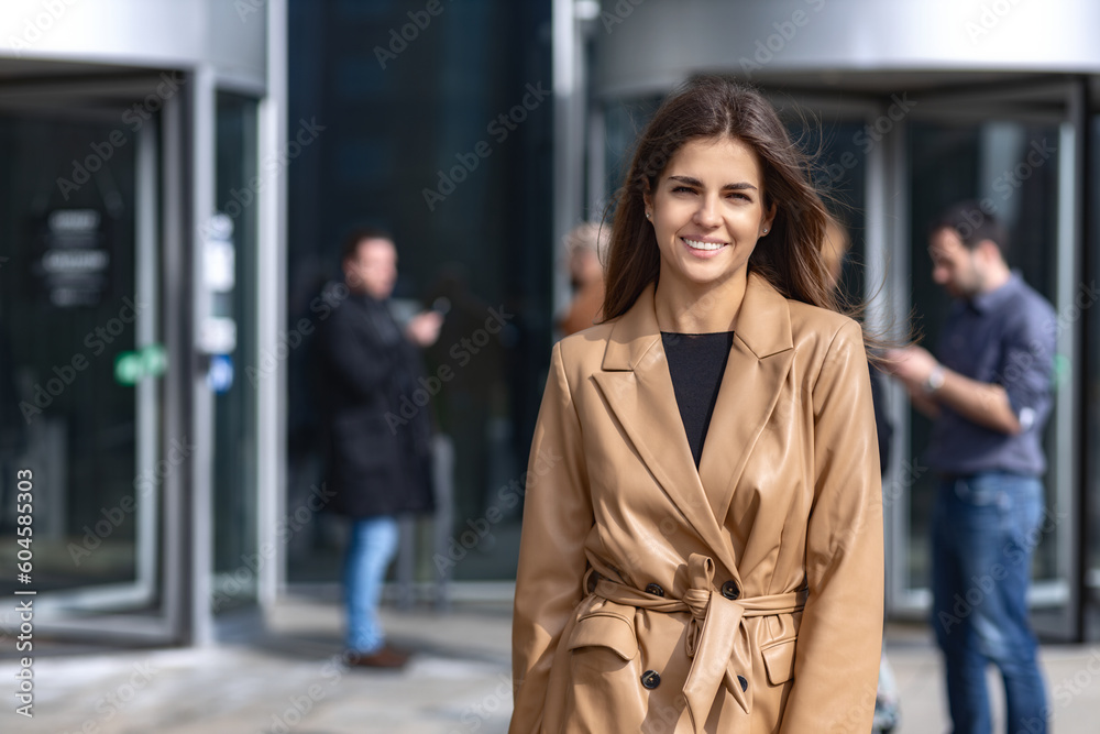 Young successful confident woman entrepreneur, CEO or an office worker in stylish clothes stands near the business center, looking confident at the camera and smiling