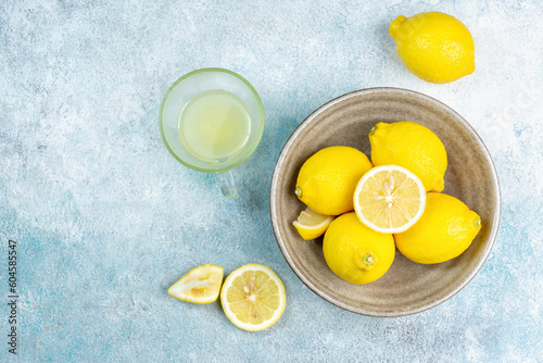 A cup of squeezed lemon juice and lemons, slices of lemons around. Bright background. Summer concept