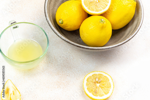 A cup of squeezed lemon juice and lemons, slices of lemons around. Bright background. Summer concept