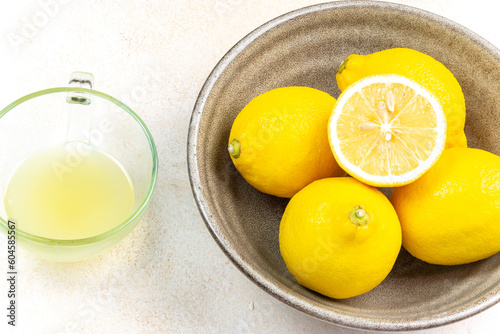 A cup of squeezed lemon juice and lemons, slices of lemons around. Bright background. Summer concept