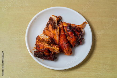 Grilled chicken in white plate on wooden table. Top view.