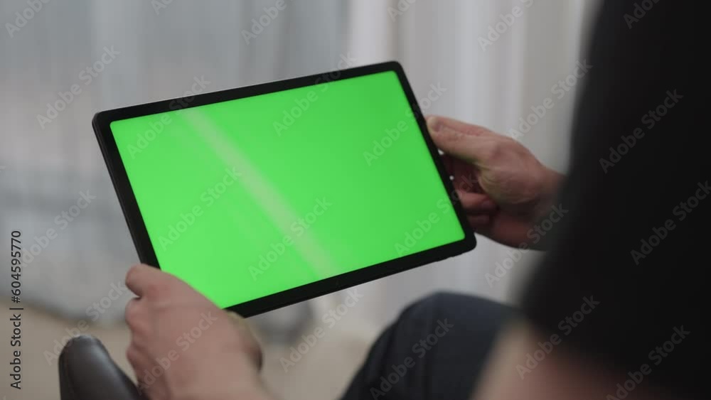 Man sitting indoors on a chair with tablet pc with green screen