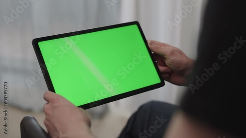 Man sitting indoors on a chair with tablet pc with green screen