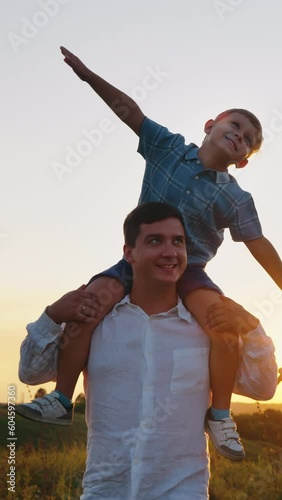 Vertical Screen: Cheerful family spending time together in countryside at sunset in slow motion. Little boy sitting on shoulders of father and playing airplane with mother, spreading arms as if flying