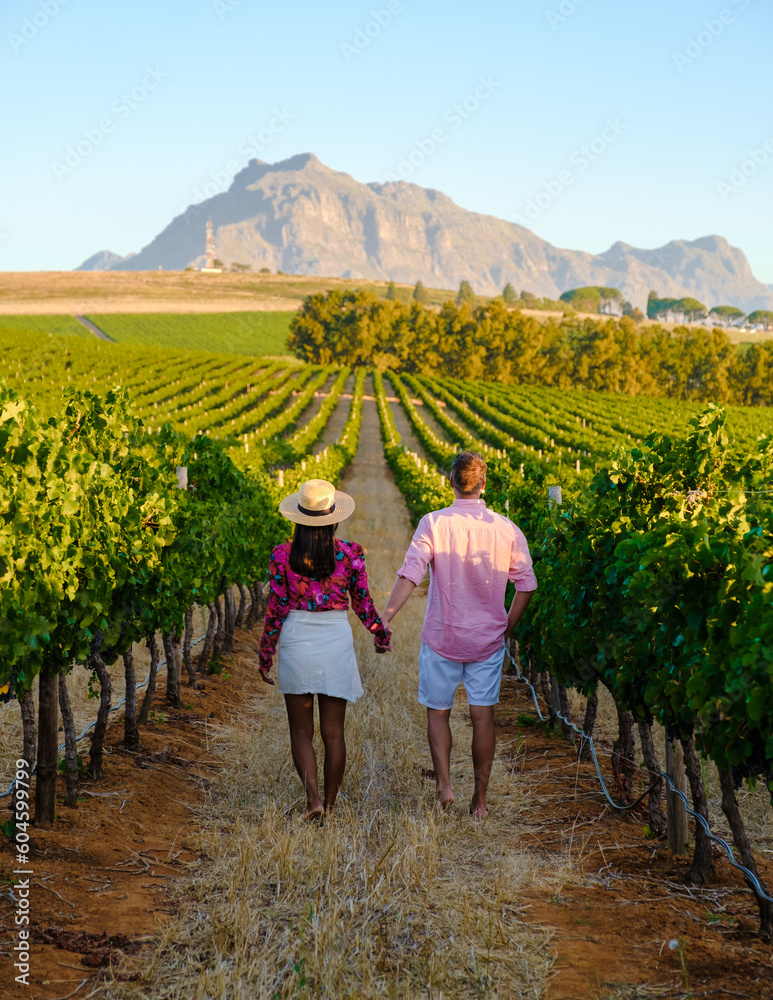 Fototapeta premium A couple of men and women are on vacation in South Africa at a Vineyard landscape with mountains in Stellenbosch, near Cape Town, South Africa