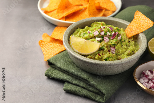 Bowl of delicious guacamole, nachos chips and lime on grey table, closeup. Space for text