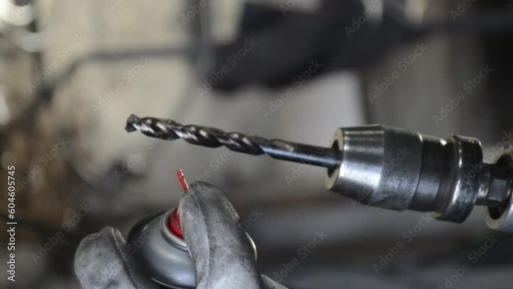 Master in protective gloves sprays with drill bit oil on a grinder