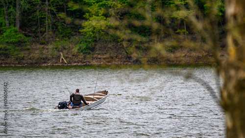 A lone man in a boat seems to be low in the water as he uses his motor to cross the choppy waters of this lake. Fisherman heading out for a day of fun with fishing poles at the ready. 