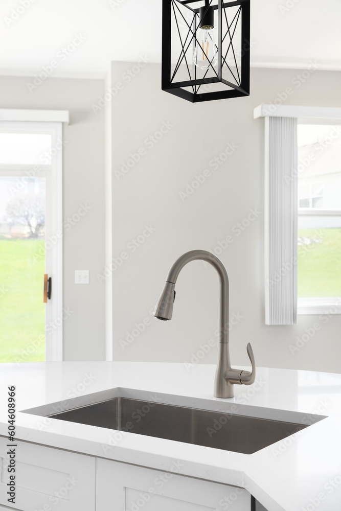 A kitchen sink detail with a black light hanging above the white island and marble countertop. A kitchen sink detail with a black light hanging above the white island and marble countertop.