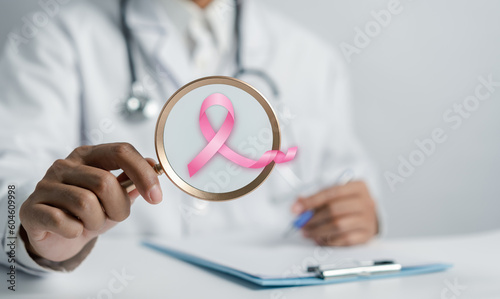 Doctor holding magnifier focus to virtual pink ribbon cancer, Breast cancer awareness and health care medical check-up concept.
