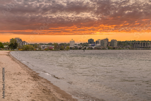 Experience the serene beauty of a sunset over Downtown Barrie's Central Park Beach in this stunning image. A lone figure riding the gentle waves adds a dynamic touch to the tranquil shoreline, paintin photo