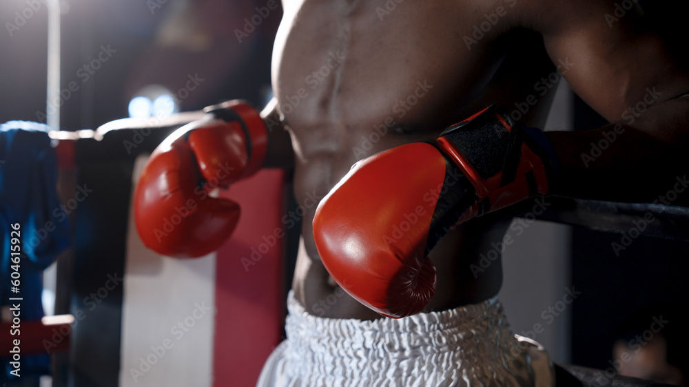 African man wearing gloves on both hands of boxer is using both arms on edge of ring. In relaxed position, breathing heavily with exhaustion after finishing boxing practice. standing in boxing ring