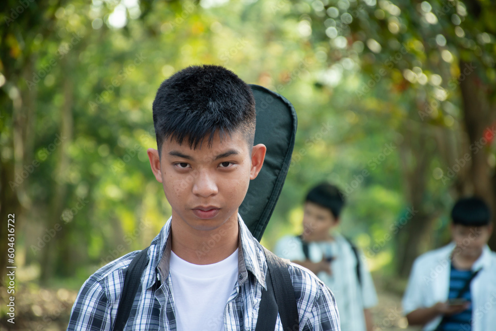 Portrait of young asian boy with black guitar back on his back, standing in front of his friends during the way to back home, soft and selective focus, concept for young teenager lifestyle. Portrait of young asian boy with black guitar back on his back, standing in front of his friends during the way to back home, soft and selective focus, concept for young teenager lifestyle.