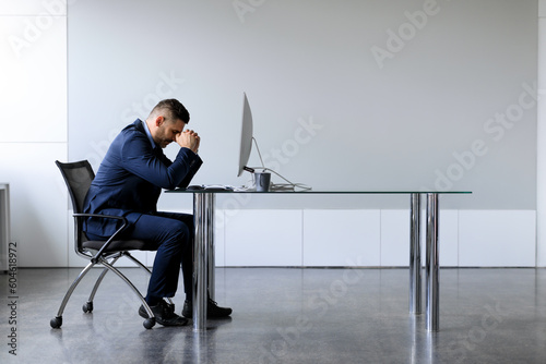Side view of middle aged office employee feeling tired of working overtime, sitting at desk with computer, copy space