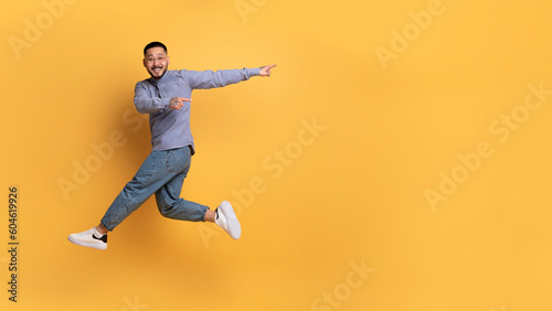 Look At This. Cherful asian man pointing aside while jumping in air