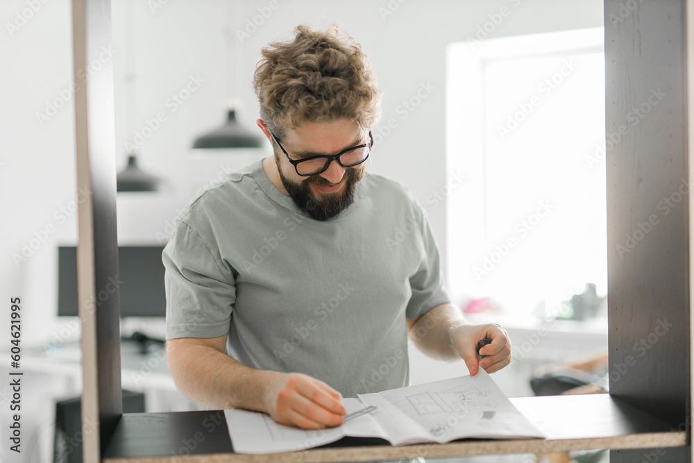 Fototapeta premium Bearded millennial man assemble his bookcase. He uses tools for furniture. Furniture for the interior room or apartments