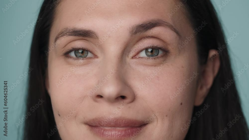 Beautiful eyes of a young woman. Close up of a woman's face with clean, healthy skin on a blue background. Good vision and eye care. Contact lenses. Natural female beauty. Slow motion.