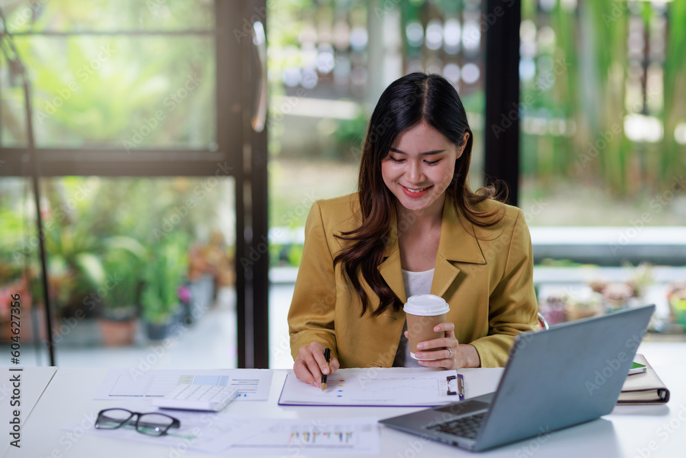 Concept of business office woman working,Businesswoman smile while working about her invesment plan with analyzing document and business investment graph data by using laptop on desk in workstation.