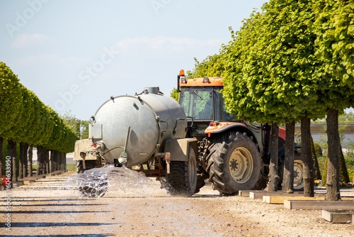 A tractor is parked on a dirt road and the tractor is carrying a tank of liquid.