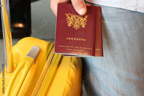 Dutch citizen Hand holding Netherlands Passport with yellow Suitcase waiting at terminal airport. photo