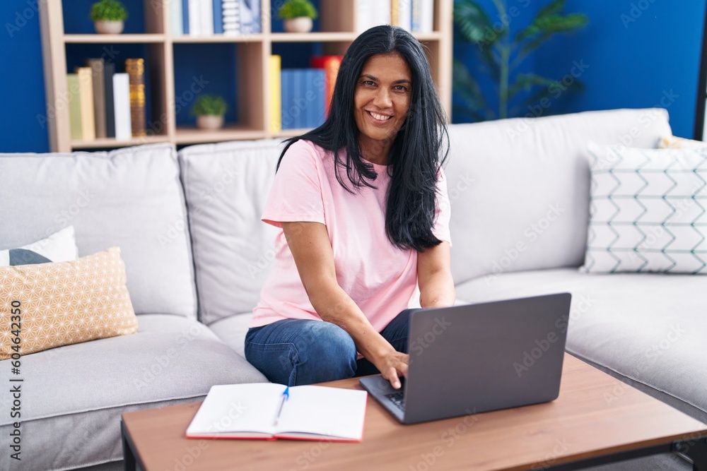 Middle age hispanic woman using laptop sitting on sofa at home Middle age hispanic woman using laptop sitting on sofa at home